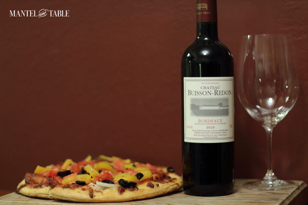 Chateau Buisson-Redon pizza wine bottle with empty wine glass on the right and pizza on the left.