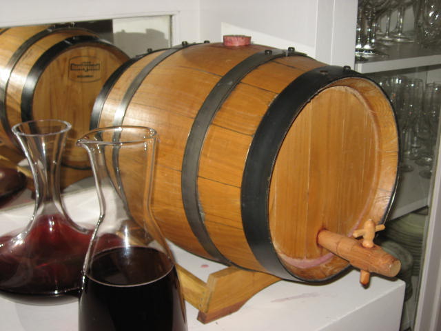 Small wooden wine barrel on the counter with two carafes of red wine ito the left.