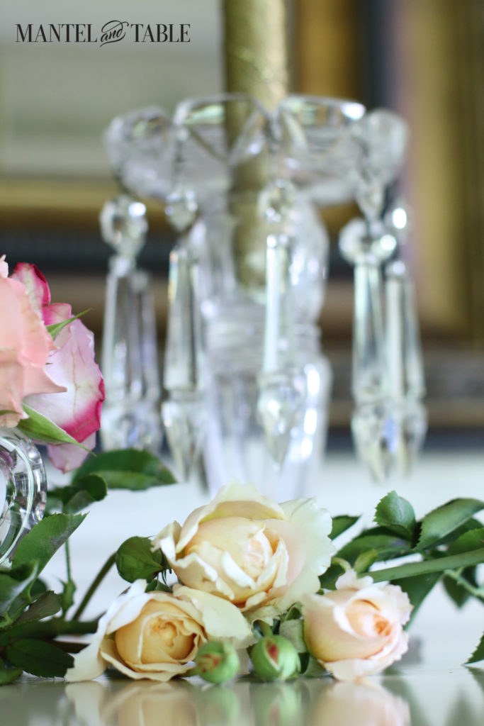 Cream garden roses lying on the mantel, crystal chandelier candlestick in the background.