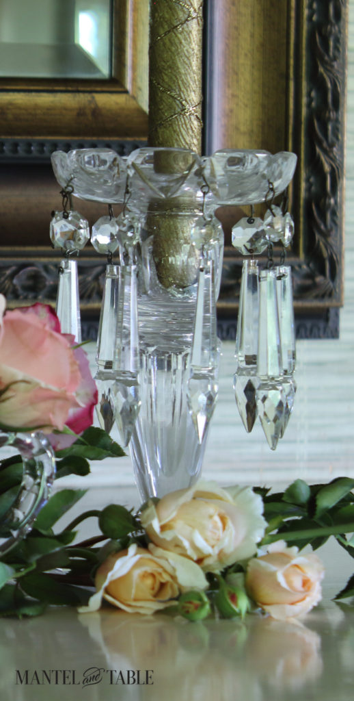 Cut crystal chandelier drop candle holders with cream roses lying on the mantel in the foreground.