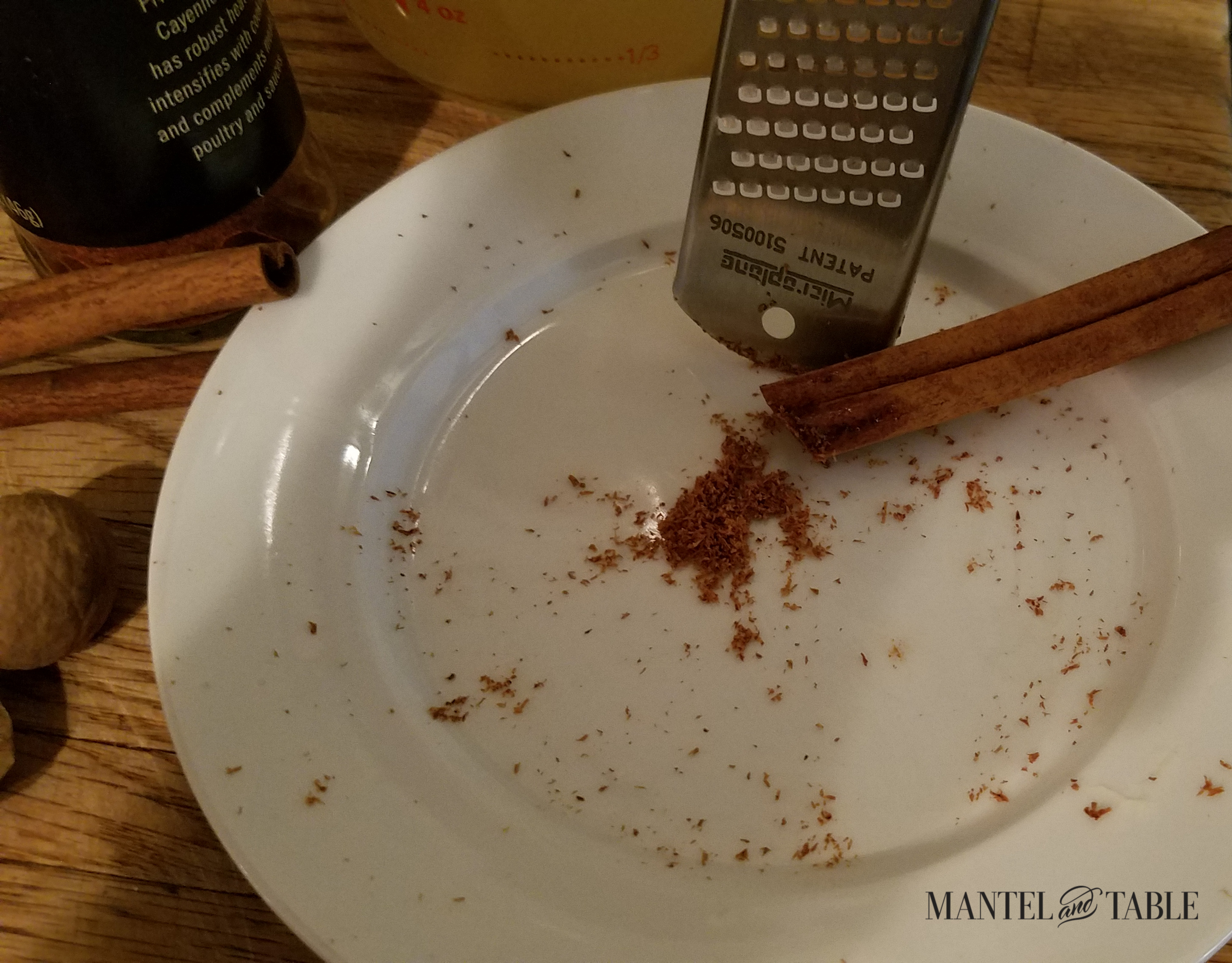 Cinnamon stick and spice grater on white plate.