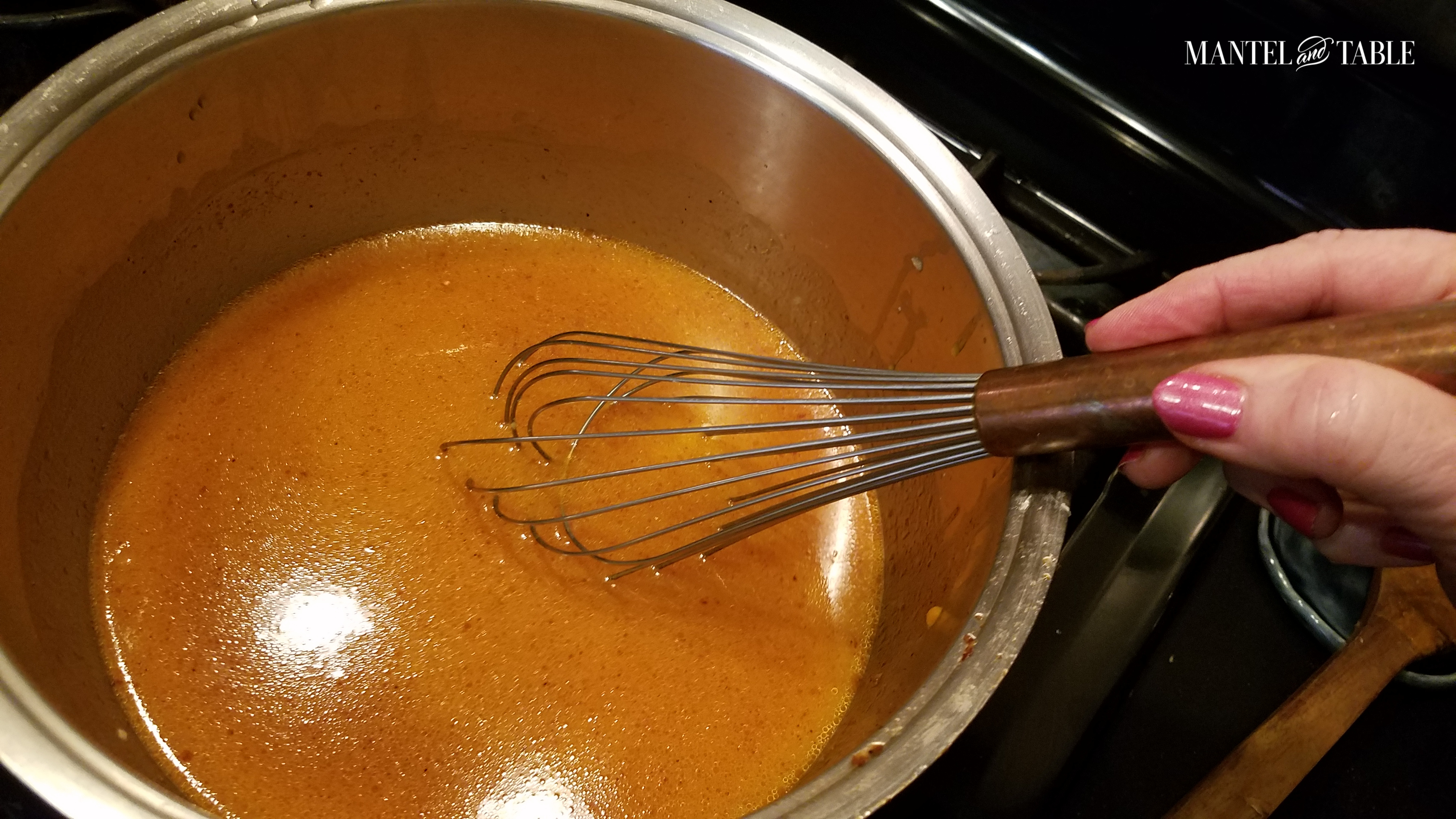 Silver pot of orange soup with copper wisk.