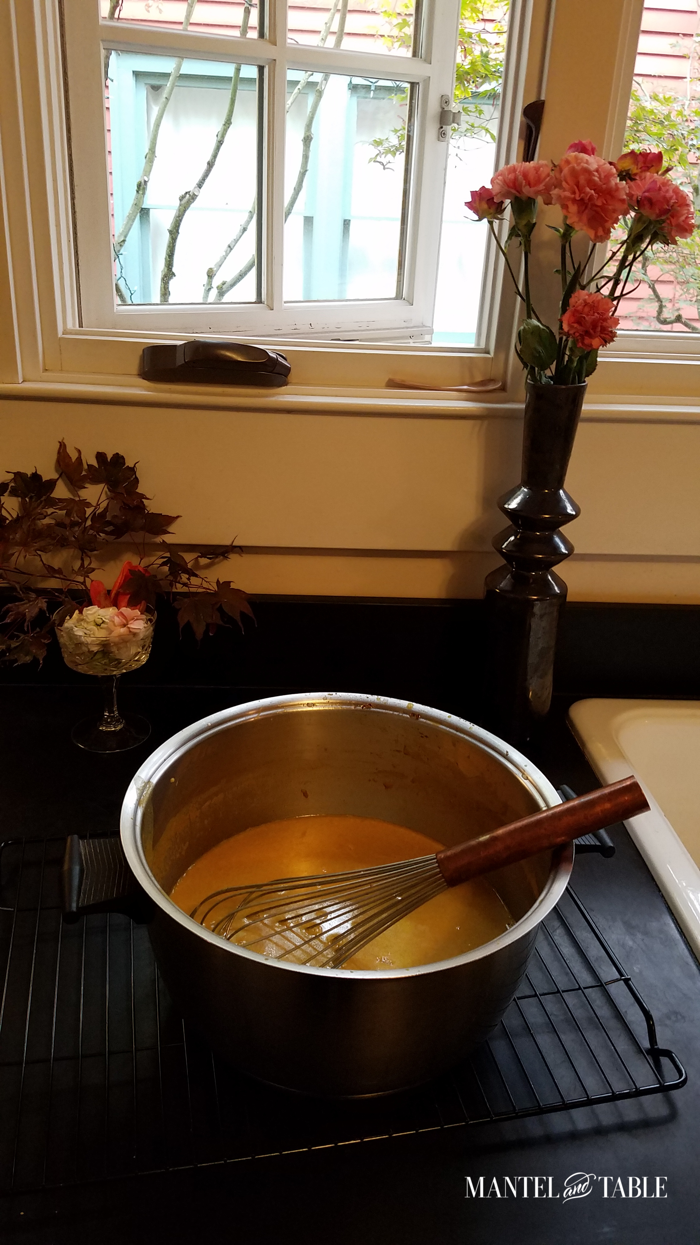 Big silver pot of orange soup on black counter in front of an open window to cool