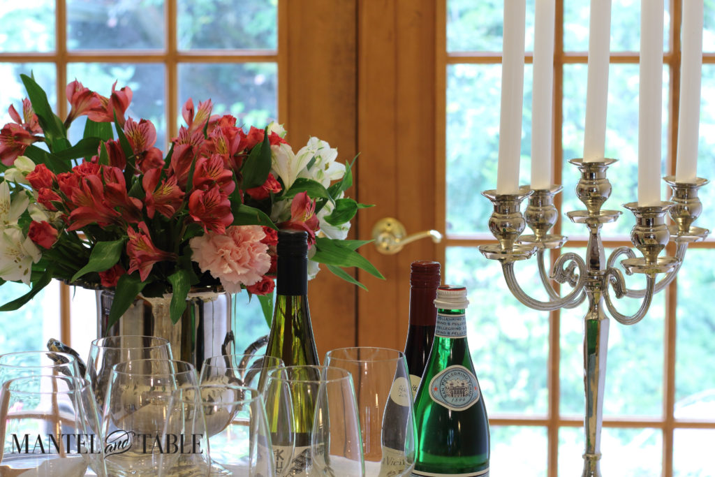 PInk Flowers in a silver wine bucket, silver candleabra, wine bottles, bottled water, and wine glasses