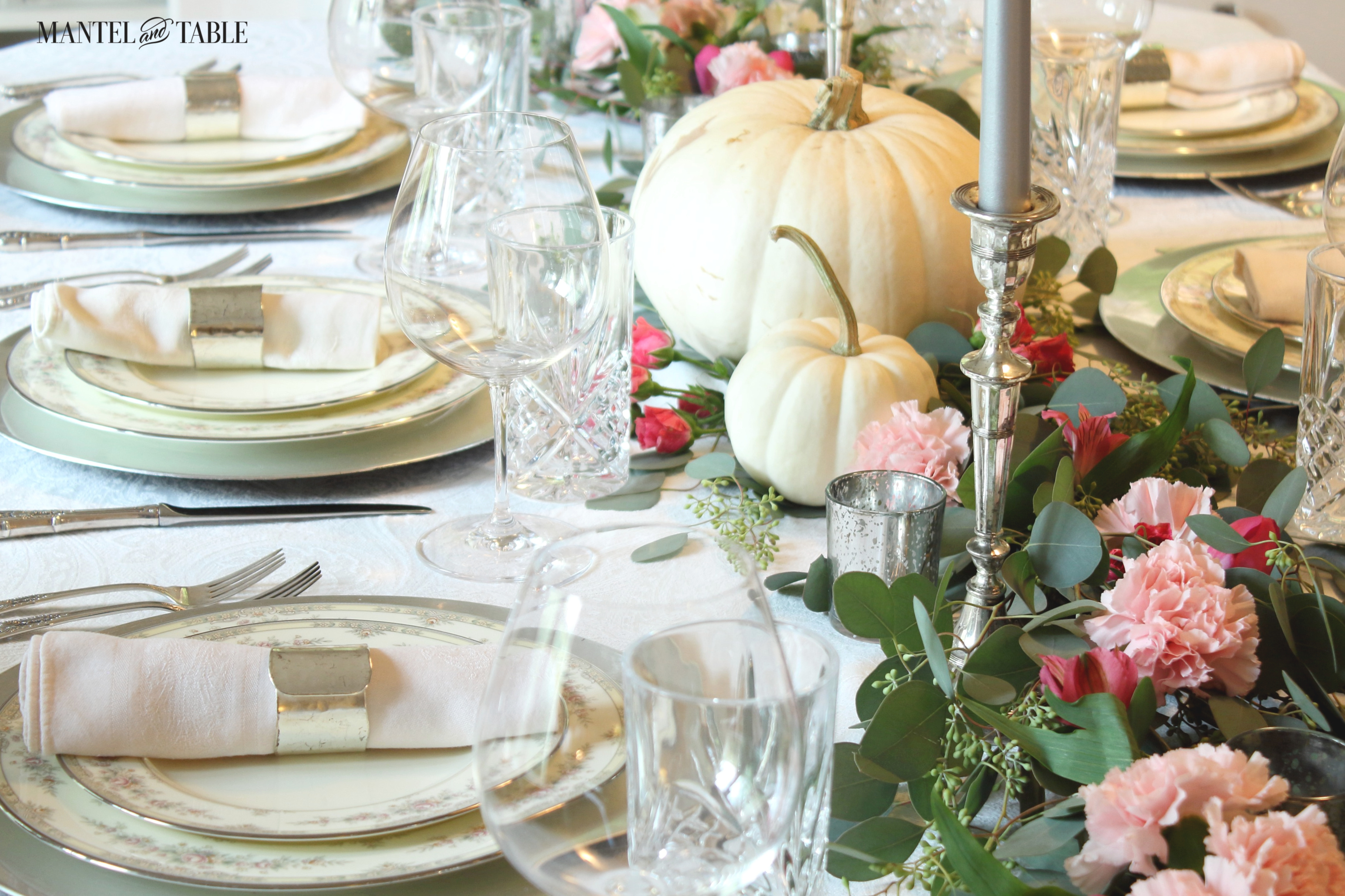 Top 10 Posts 2019 ~ Close shot of china with pink flowers on silver chargers. Blush linen napkins rolled in sleek silver rings. White pumpkin & pink flower garland w/silver candles.