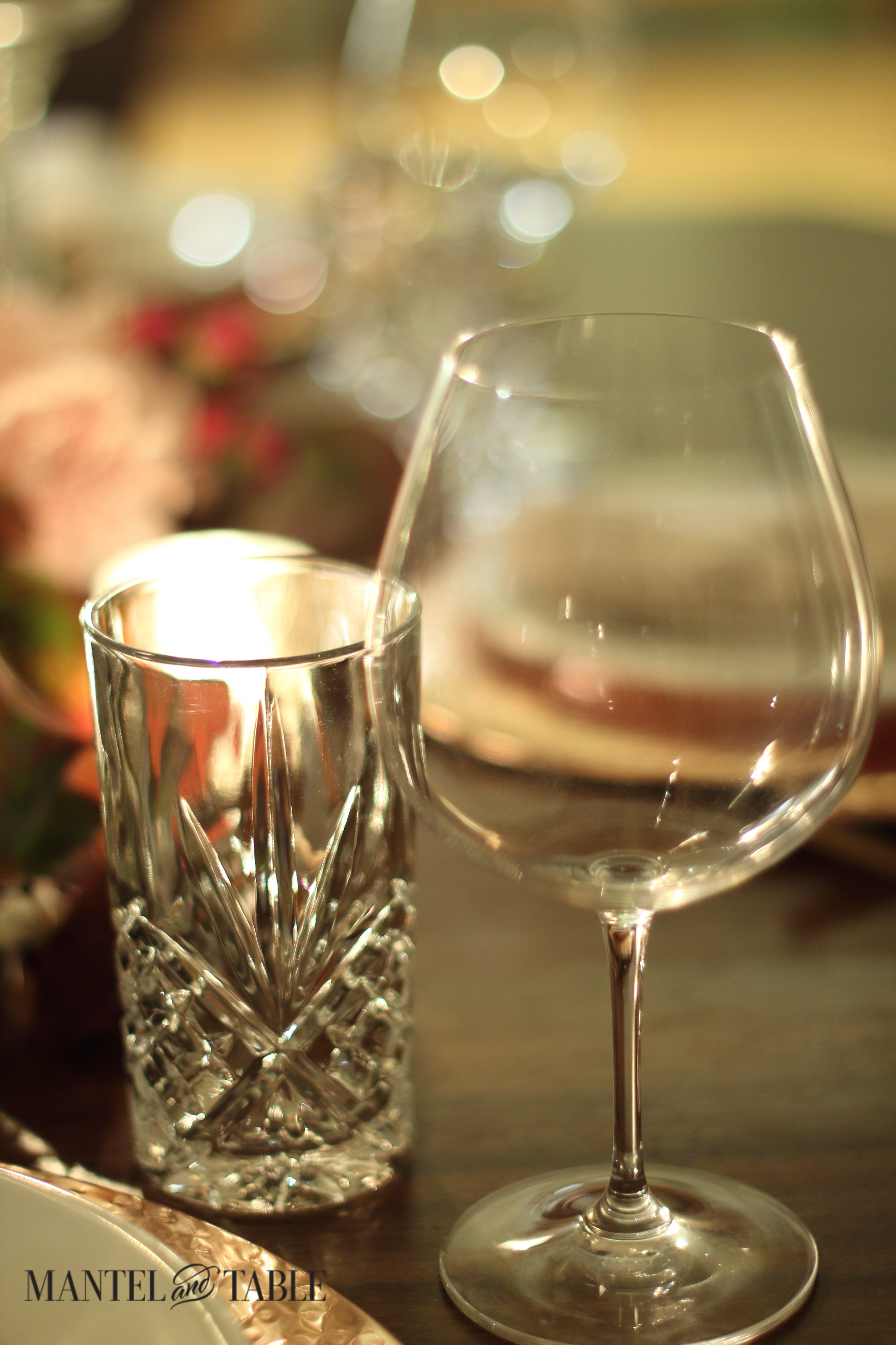 Cut crystal water glasses & round-bottom Riedel wine glass with soft focus pink flowers behind.