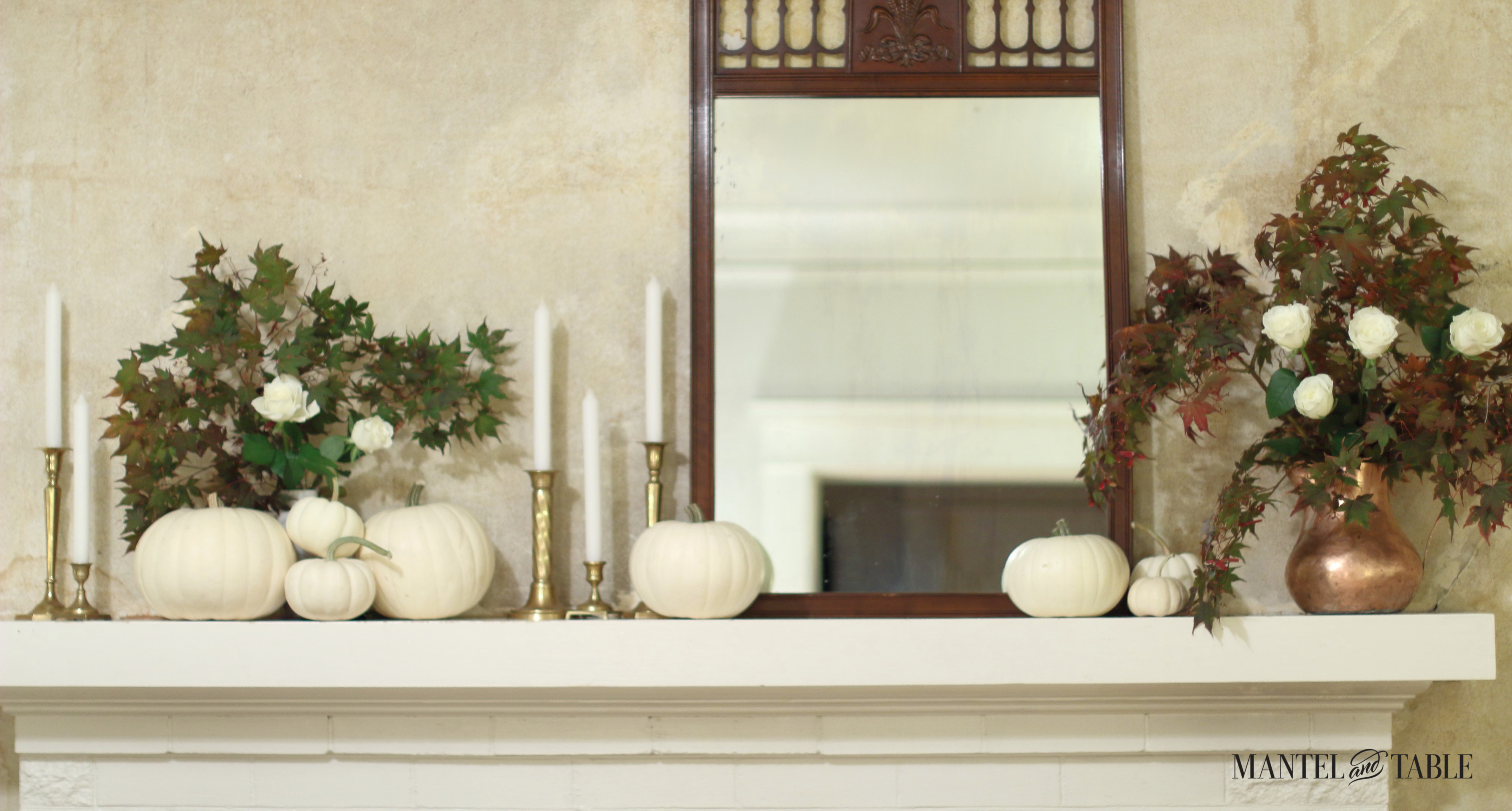 White pumpkins of many sizes on the white mantel. Lovely lattice topped wood dark wood mirror, brass candlesticks with white candles. Red and green maple leaves in a copper pitcher with white roses.