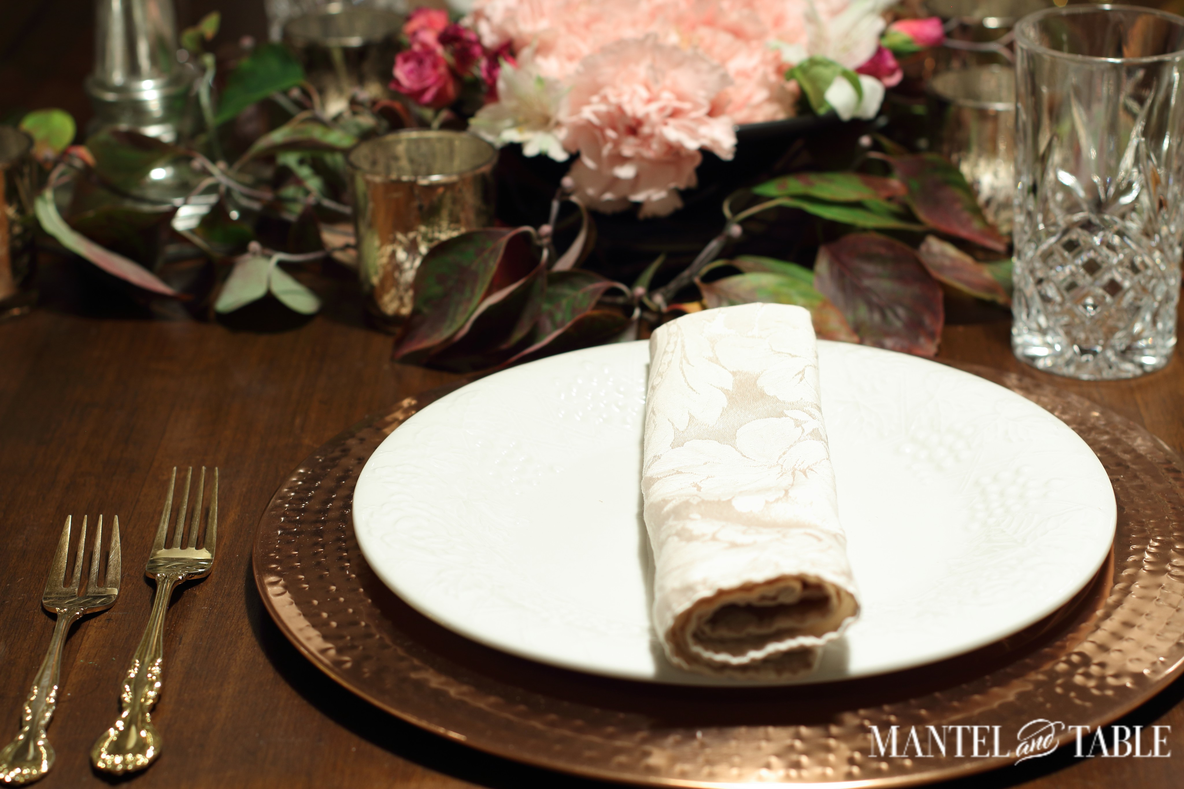 light blush napkin on white plate & copper charger. Pink flower arrangement in the background.