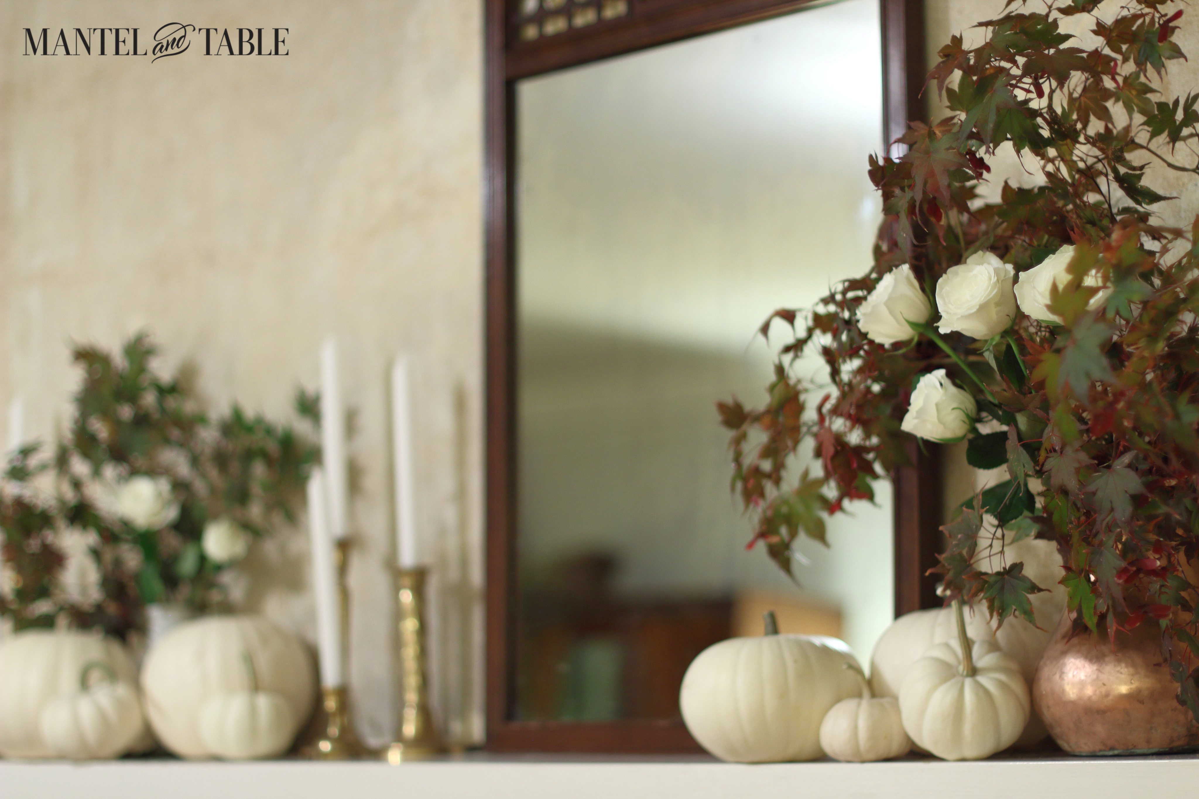 White mantel closeup, at an angle, with white pumpkins, maple leaves & white roses. Brass candlesticks.