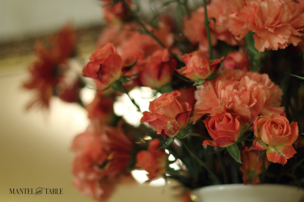 Closeup of peach carnations & dark peach baby roses in a white vase