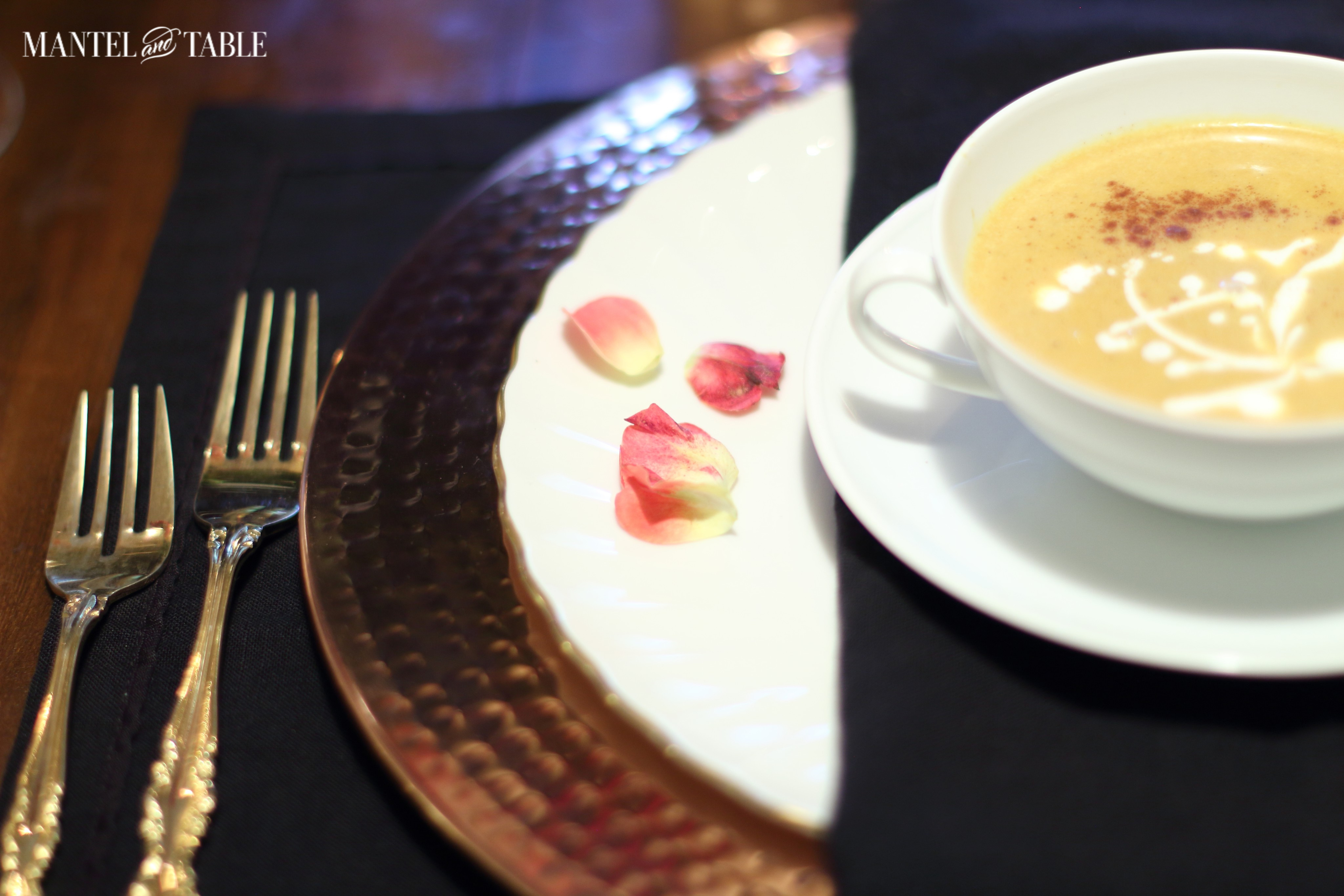 Copper charger, gold rimmed white china plate, black napkin, white soup bowl & saucer.