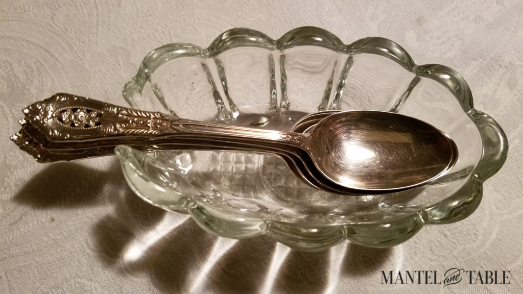 Silver teaspoons stacked in a scalloped clear glass spoon holder