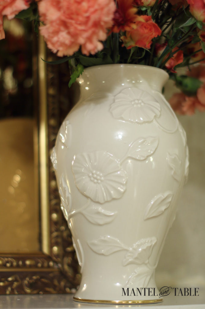 White Lenox vase with raised flower detail. Gold framed mirror behind.