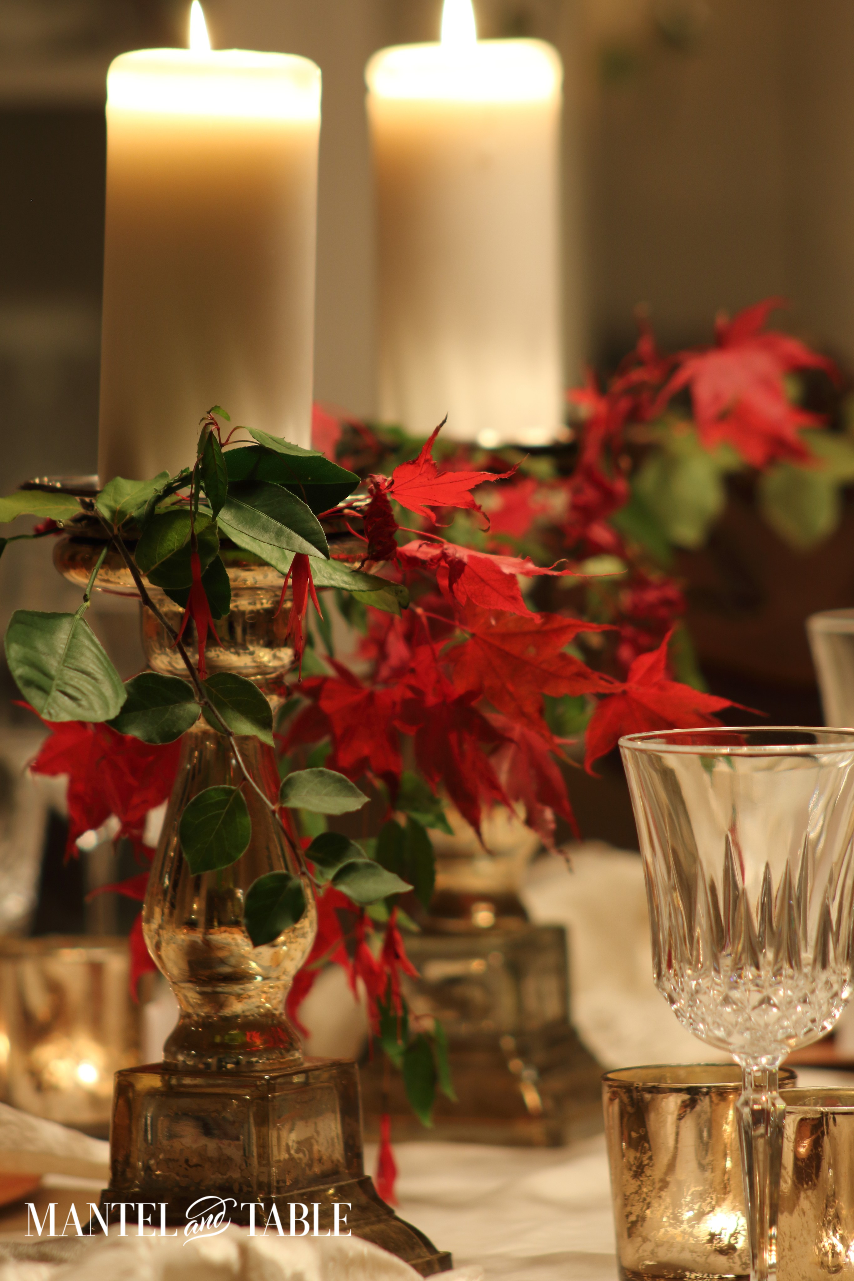 Gold mercury glass candlesticks with glowing white candles, red leaves & greenery on Thanksgiving table