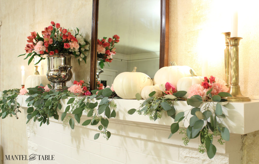 Angle shot of the white mantel with white pumpkins and pink flowers, brass candlesticks.