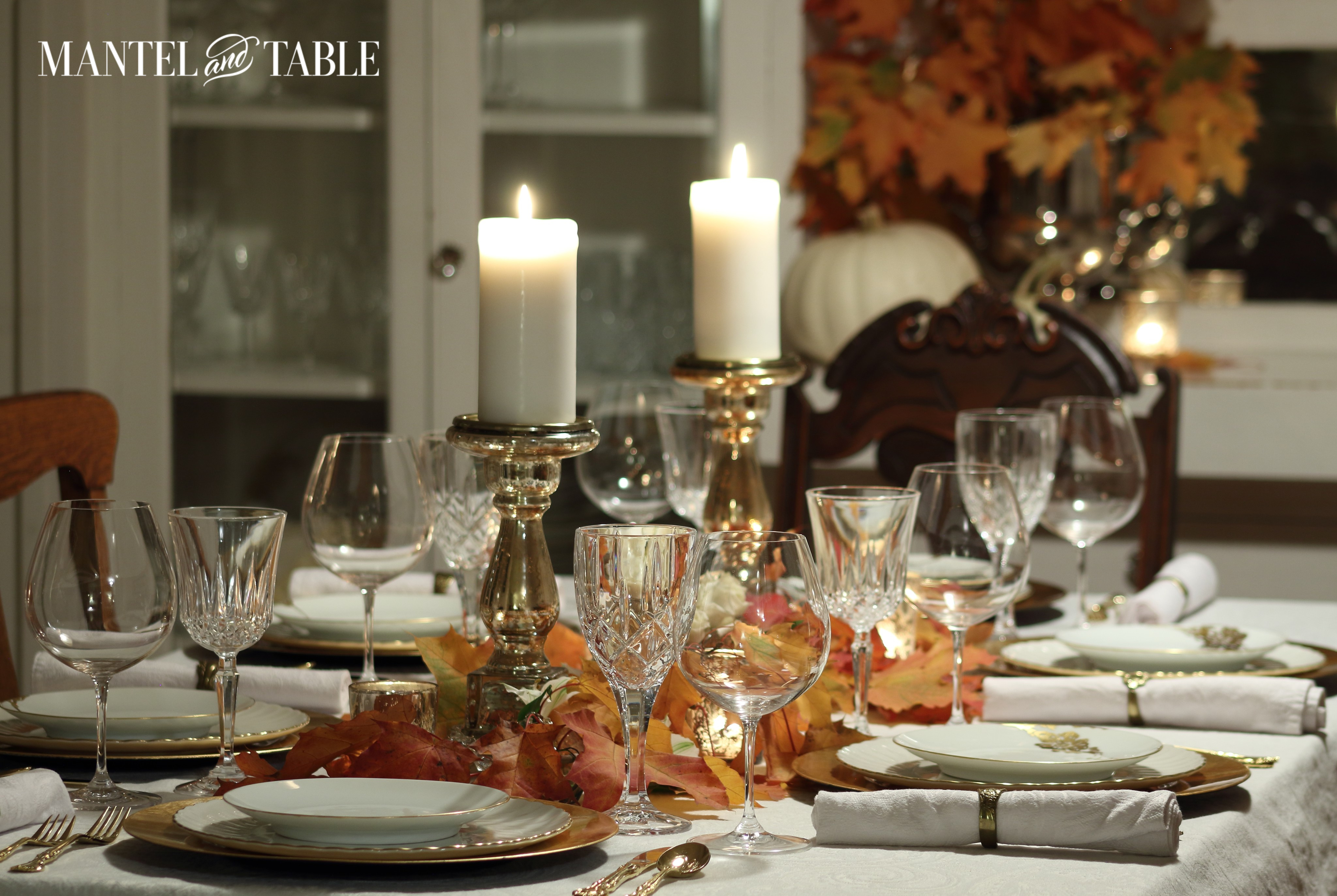 Red & orange fall leaves on white tablecloth with gold chargers & white & gold china
