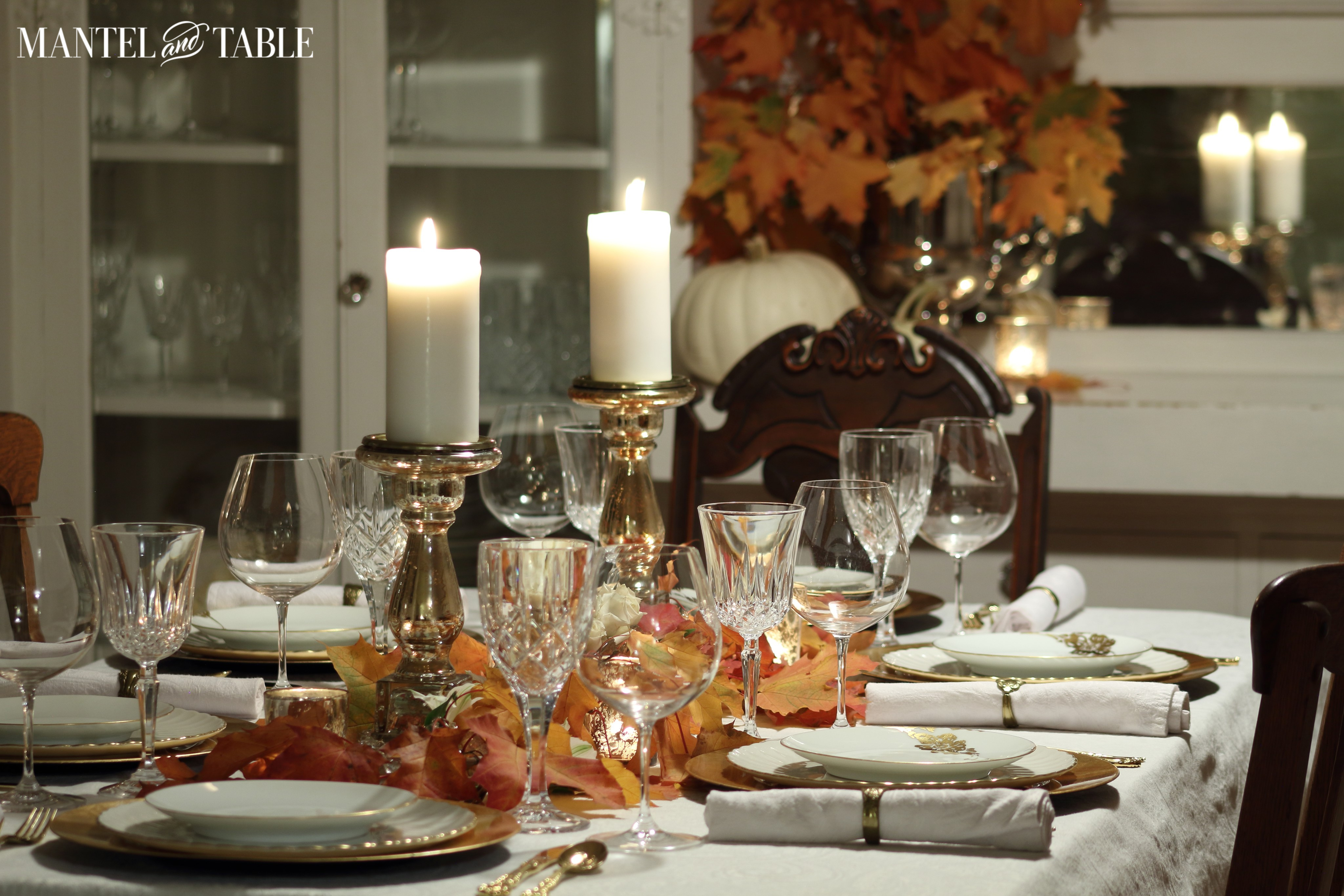 Red & orange fall leaves on white tablecloth with gold chargers & white & gold china
