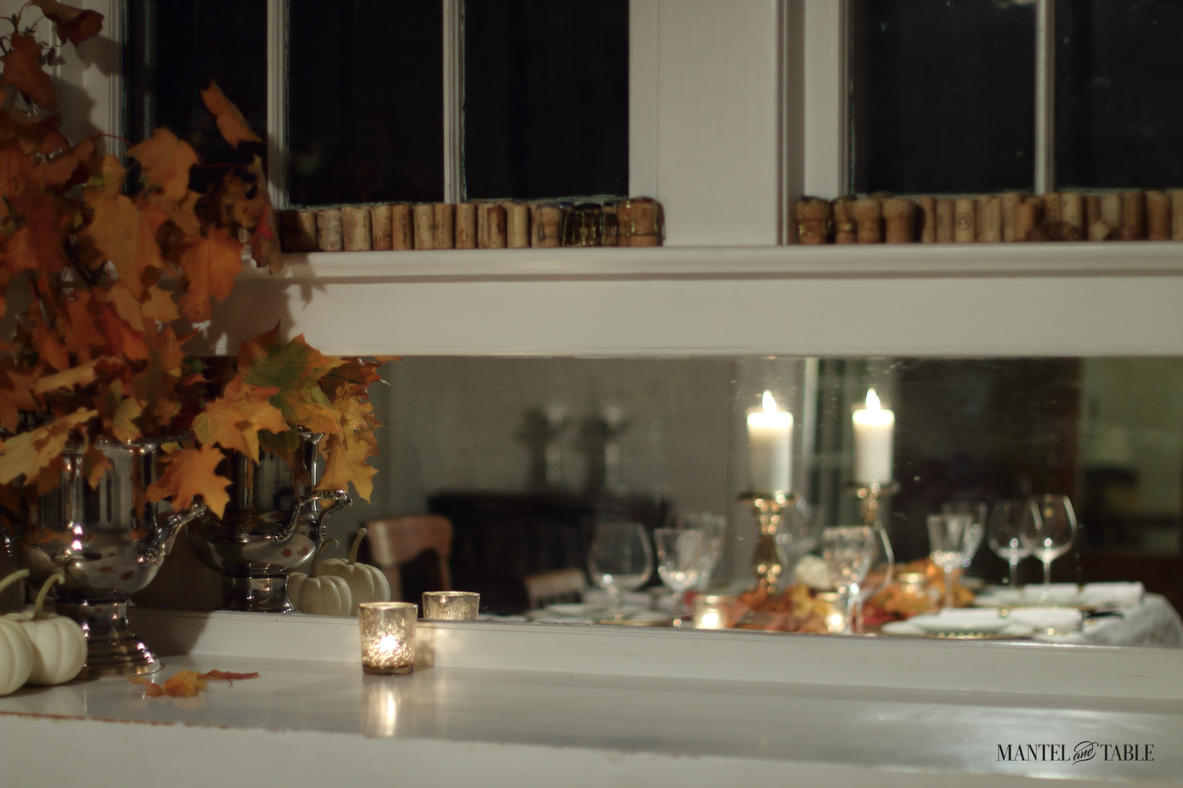Fall leaves in front of buffet mirror reflecting the white & gold tablesetting and candles.