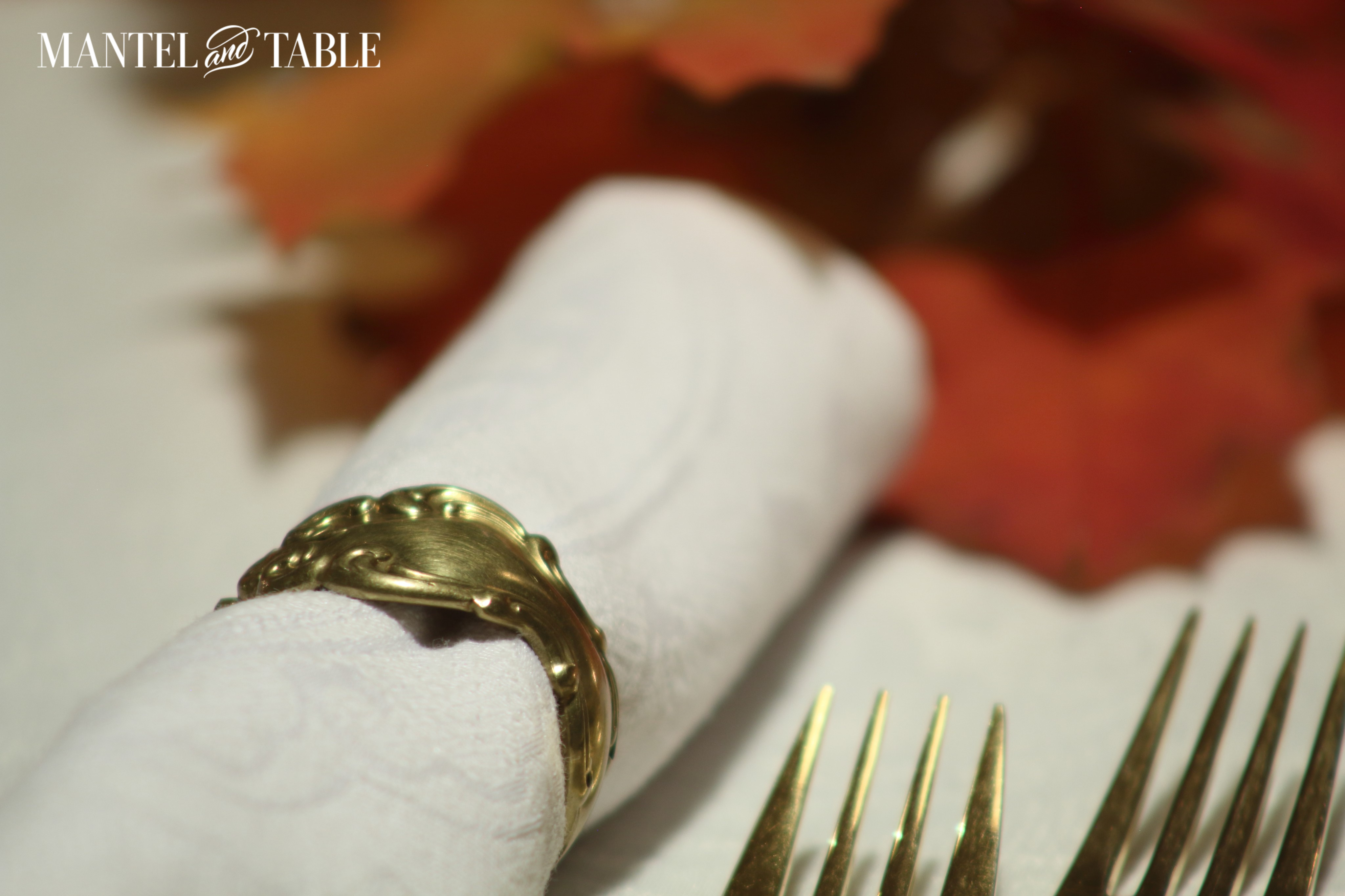 White linens, gold napkin rings, gold forks, and red leaves