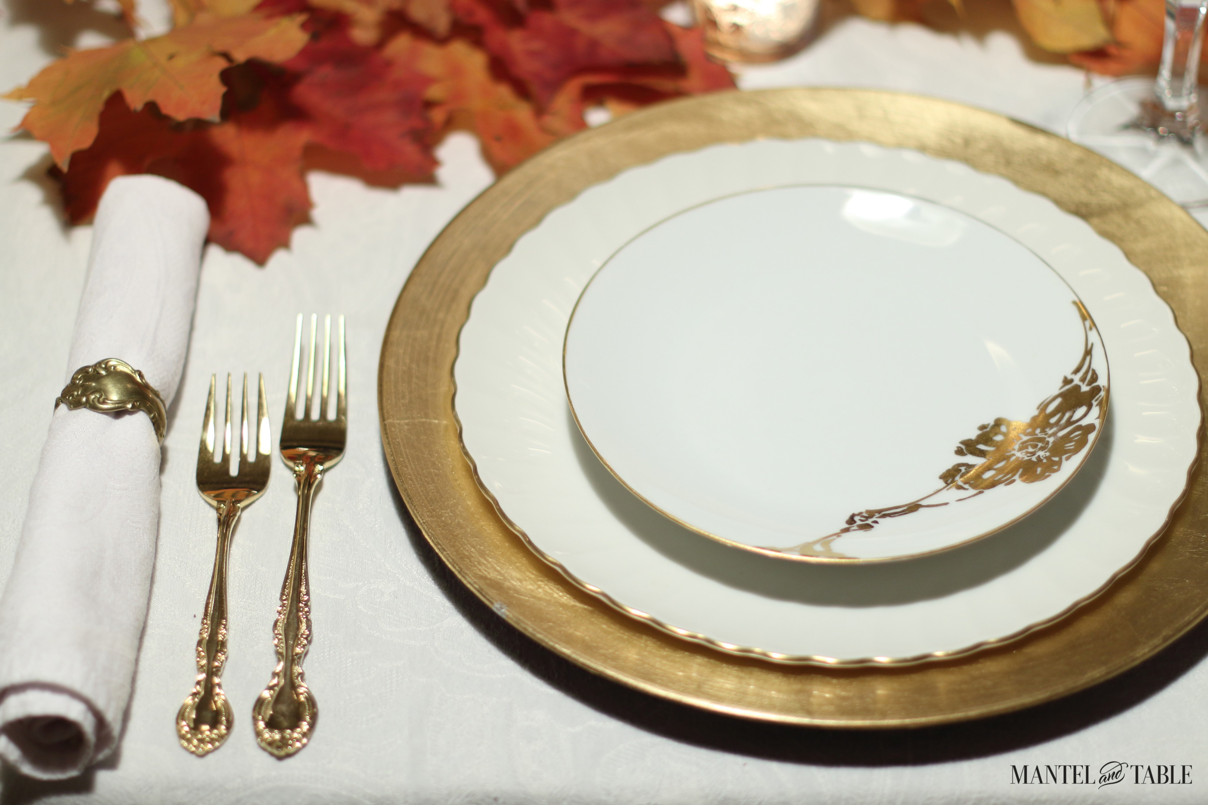 Gold plaesetting on white tablecloth with red & orange fall leaves at the top