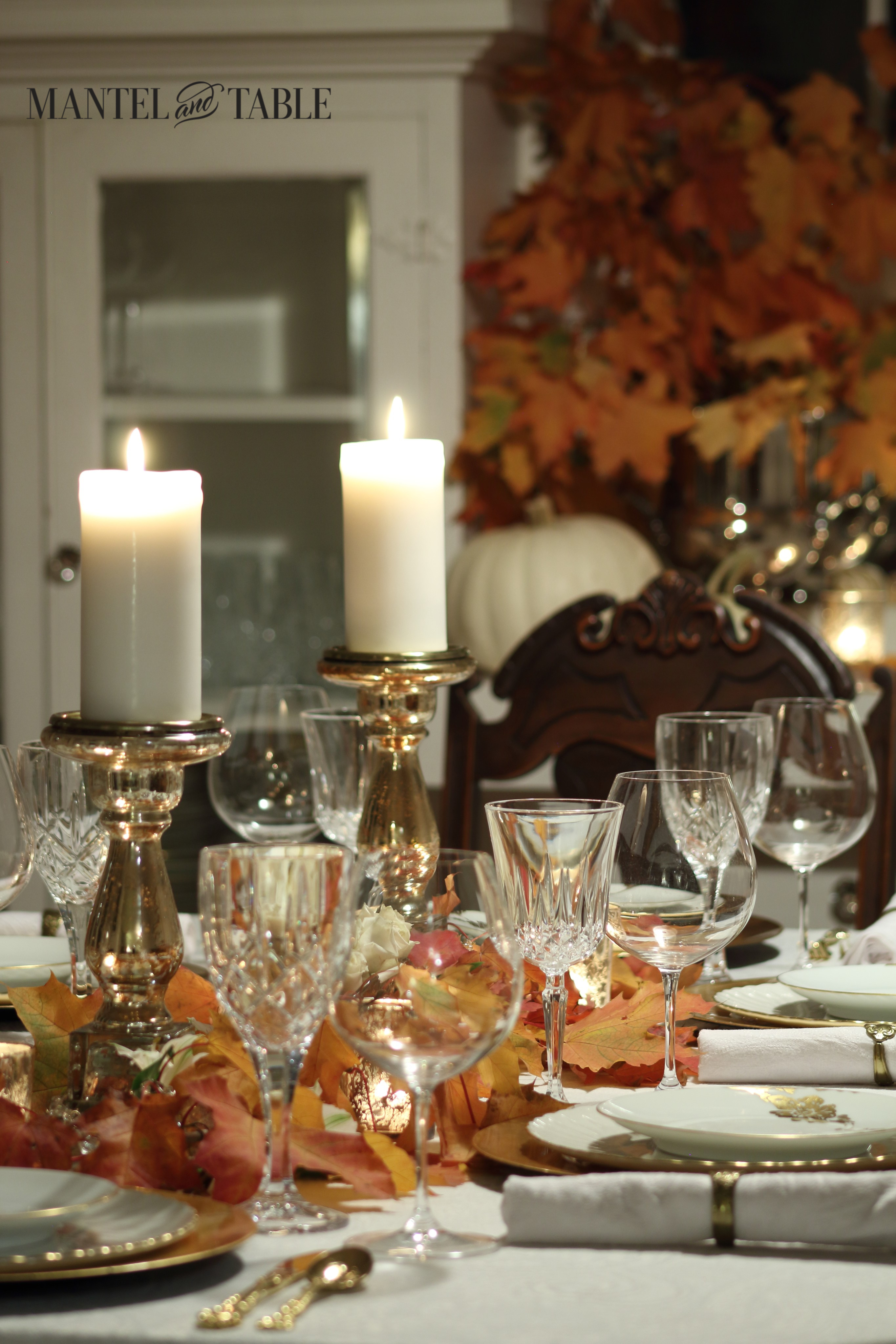 White & gold table with fall leaves, glowing candles & crystal goblets.