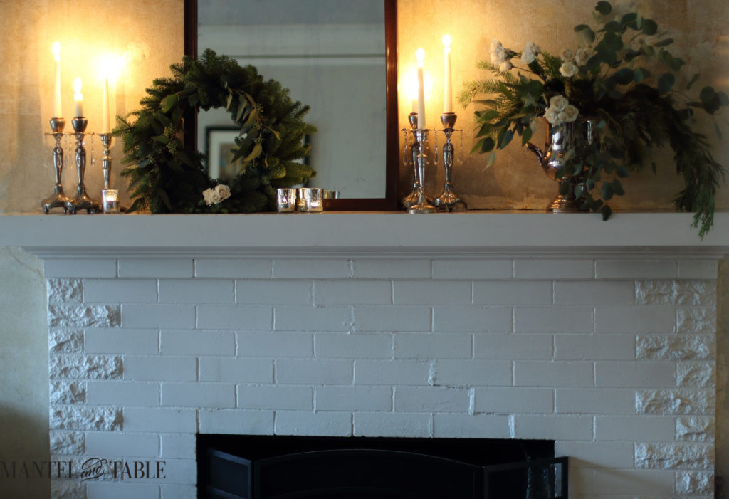 White mantel with matching evergreens & roses in candlelight