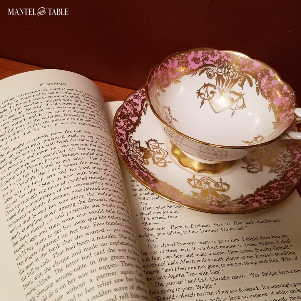 pink, gold, & white teacup on top of open book page, red wall background