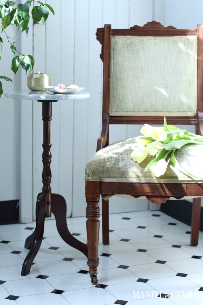Green chair with yellow tulips next to a small marble topped table with chocolates & lit candle
