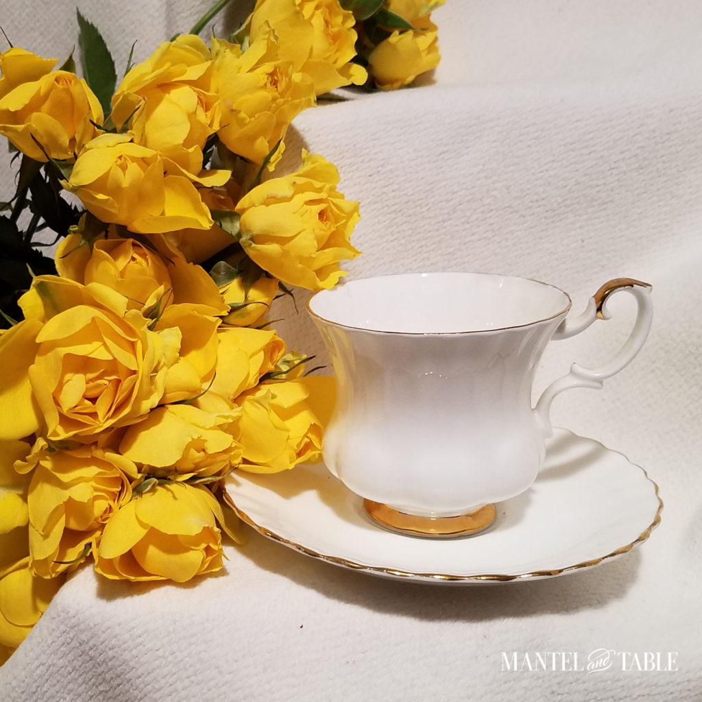 white & gold teacup on cream background with vivid yellow roses