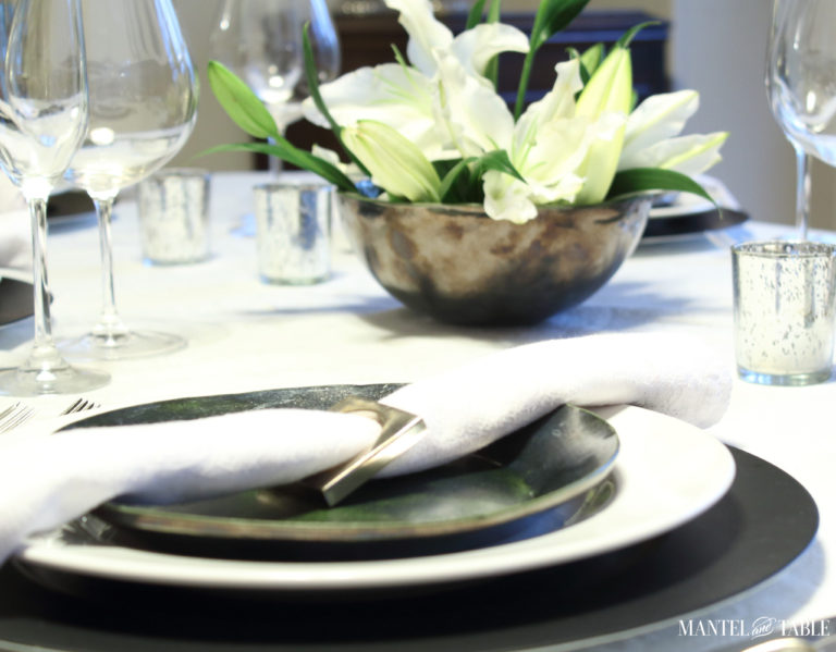 Black & white industrial table setting with centerpiece of white lilies-plate stack & flowers