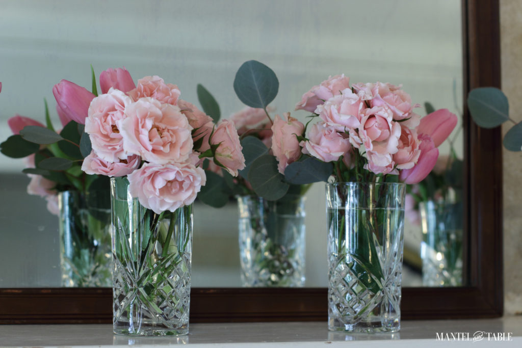 Two crystal vases with pink flowers on mantel