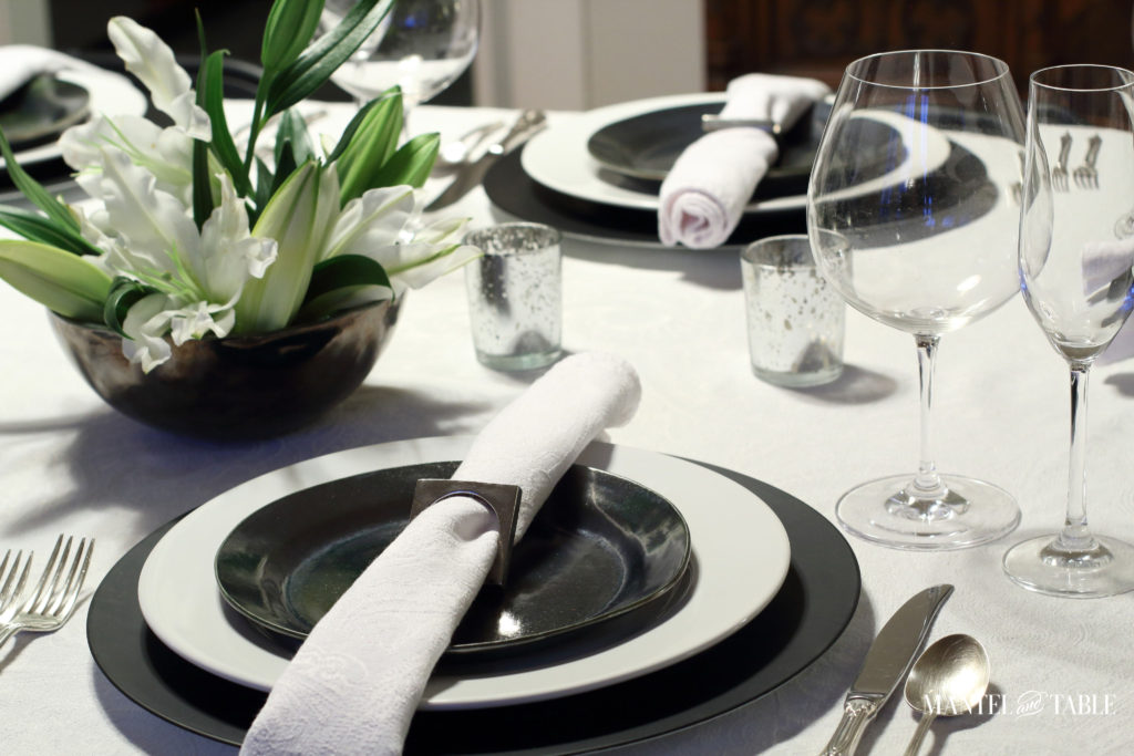 Black & white industrial table setting with centerpiece of white lilies two places across the table.