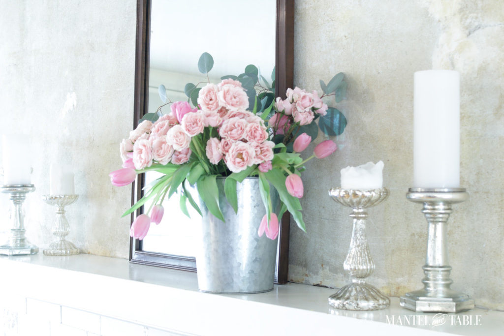 Mantle arrangement of light pink roses, dark pink tulips, eucalyptus in a galvanized bucket.. SIlver piller candlesticks, white candles