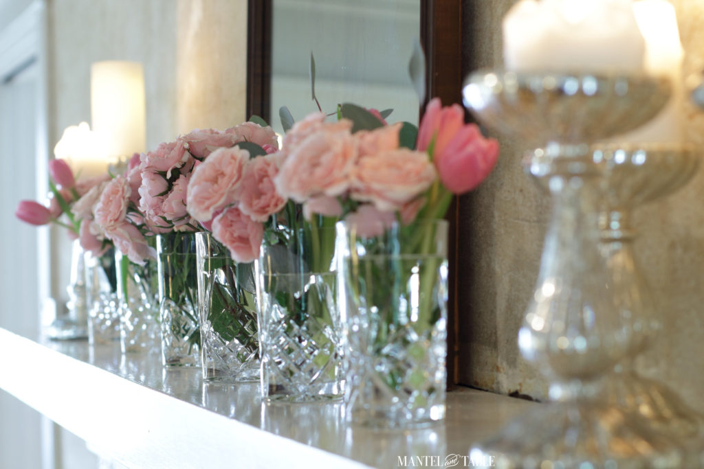 Row of crystal vases on mantel with pink flowers