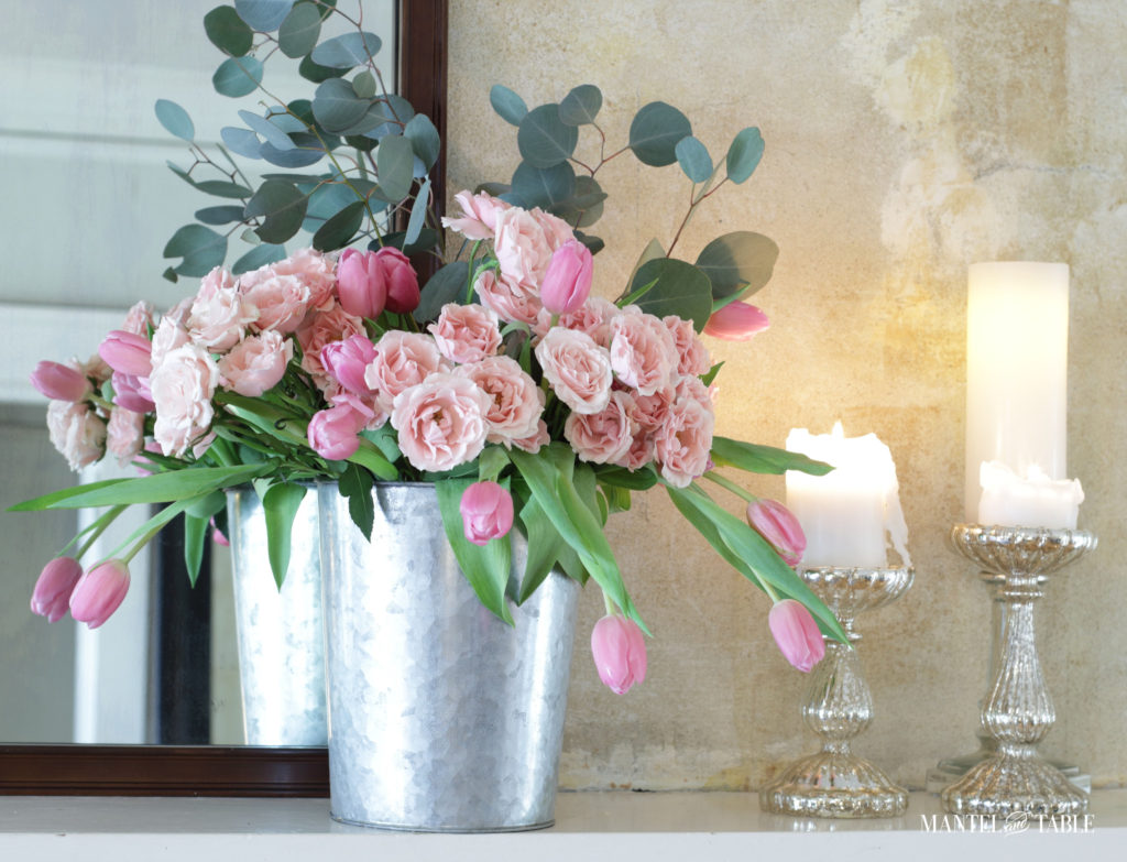 pink flowers in bucket on mantel with candles
