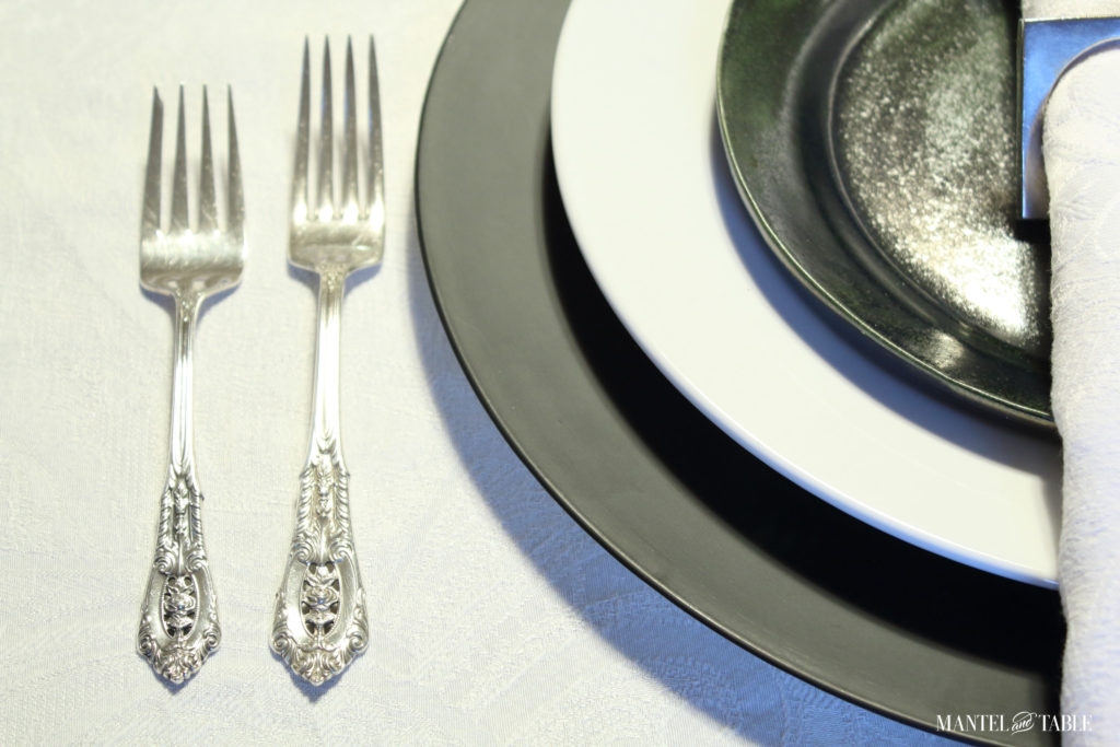 Black & white industrial table setting with centerpiece of white lilies - Plate stack & silver forks