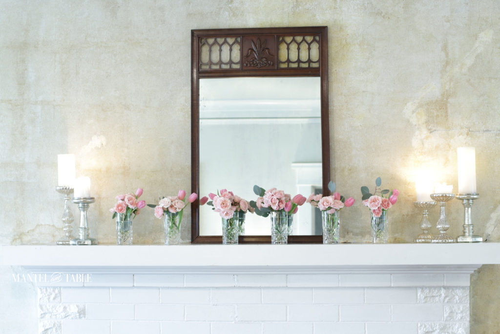 pink flowers in crystal vases on mantel. Antique mirror and candles