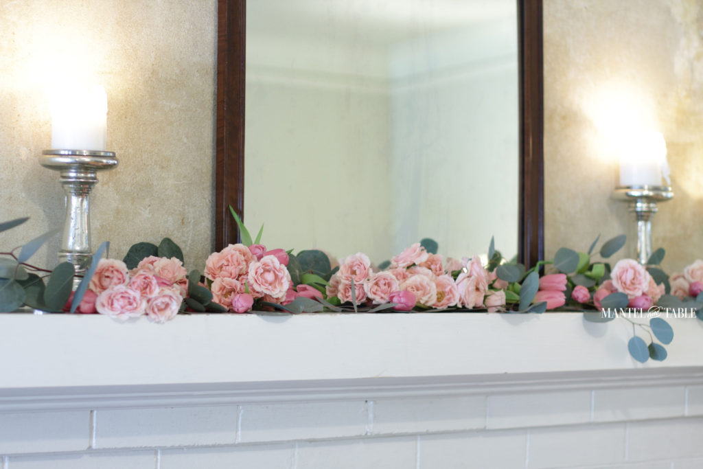Garland of pink flowers on mantel with mirror and candles
