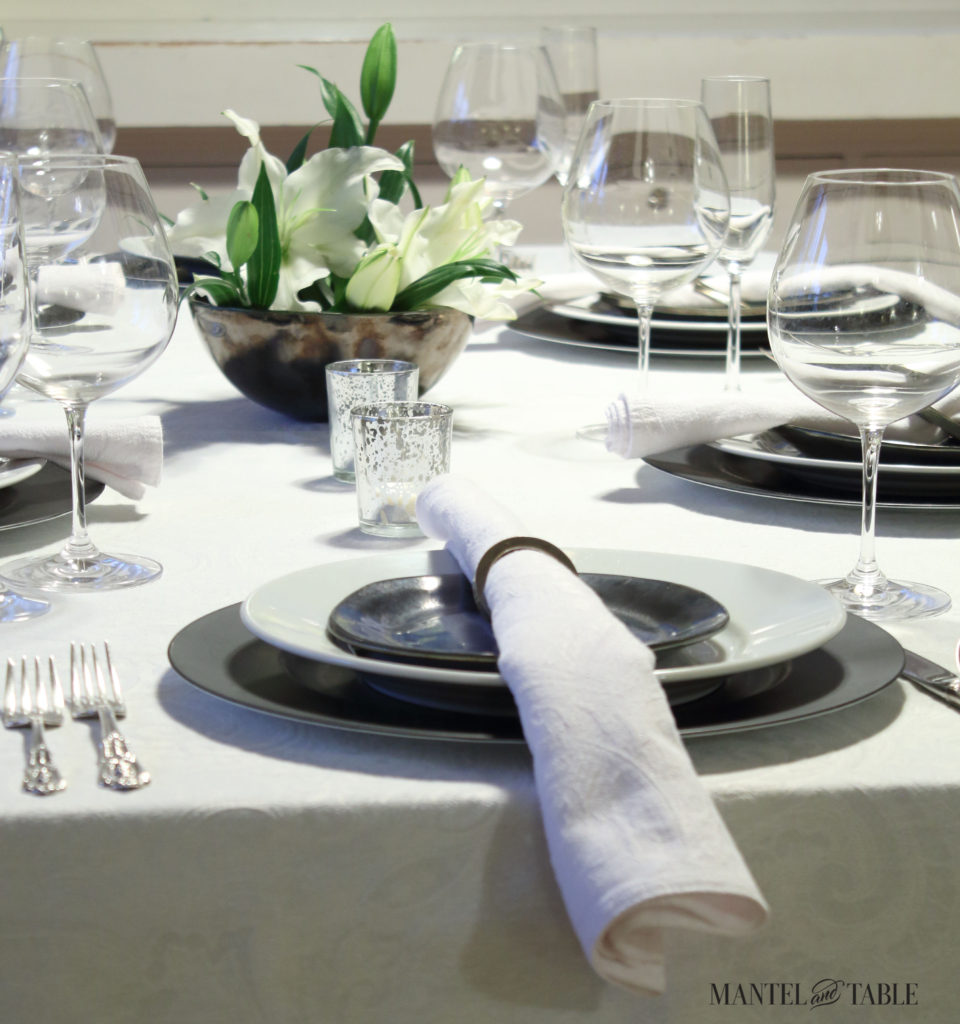 Black & white industrial table setting. with centerpiece of white lilies - view from foot of table.