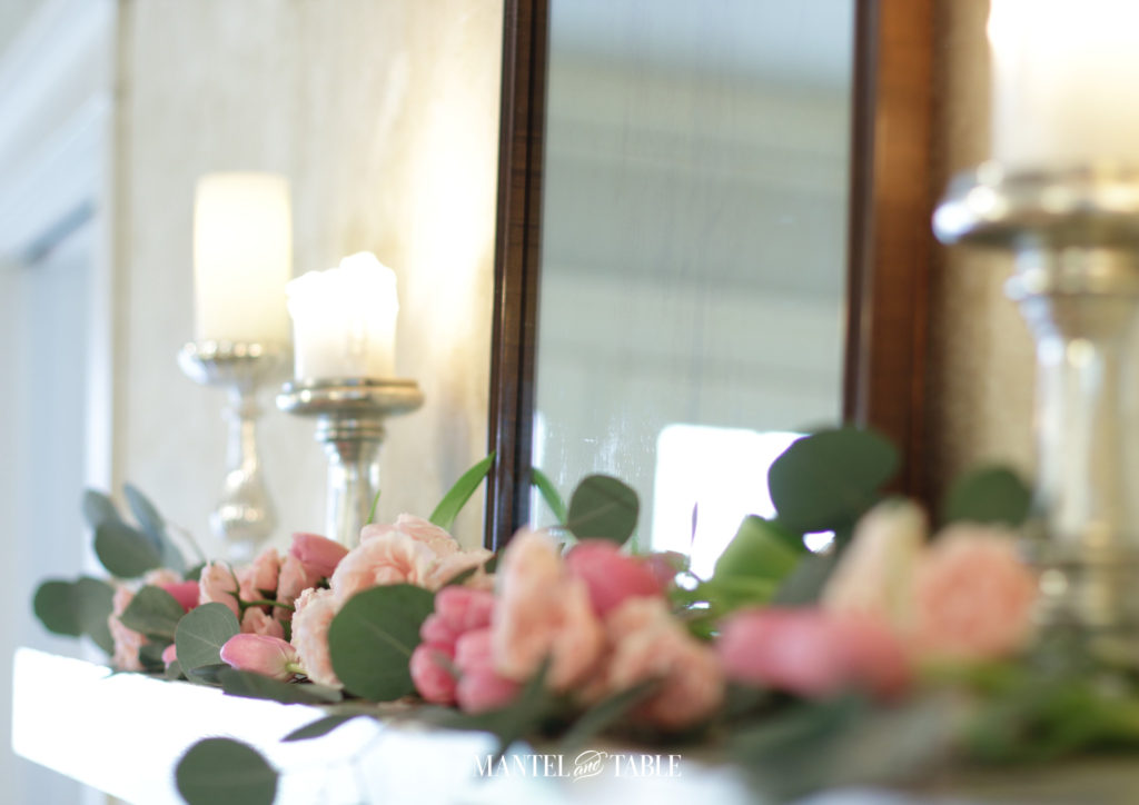 Angled soft focus pink flower garland on mantel in front of mirror. candlelight