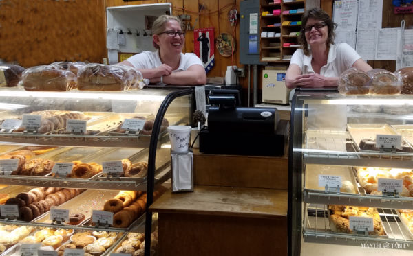 Two Bakers leaning on top of the counter full of delicious baked goods