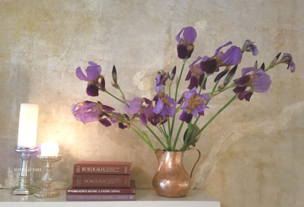 Purple iris in copper pitcher on the mantel. Purple book stack & silver candle holders.