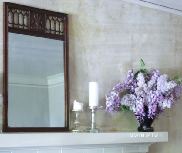Black amethyst glass vase of lavender lilacs & wisteria on white mantel with brown mirror