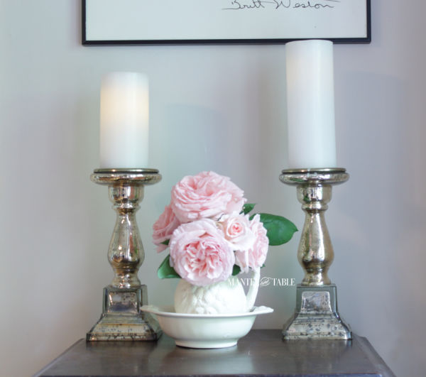 Fresh flowers - blush roses in white ceramic pitcher & bowl between two gold pillar candles.