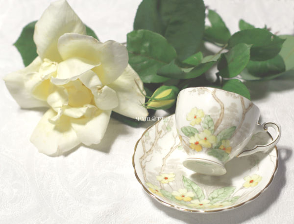 White teacup with yellow flowers and tree design on white linen with yellow fresh flower roses.