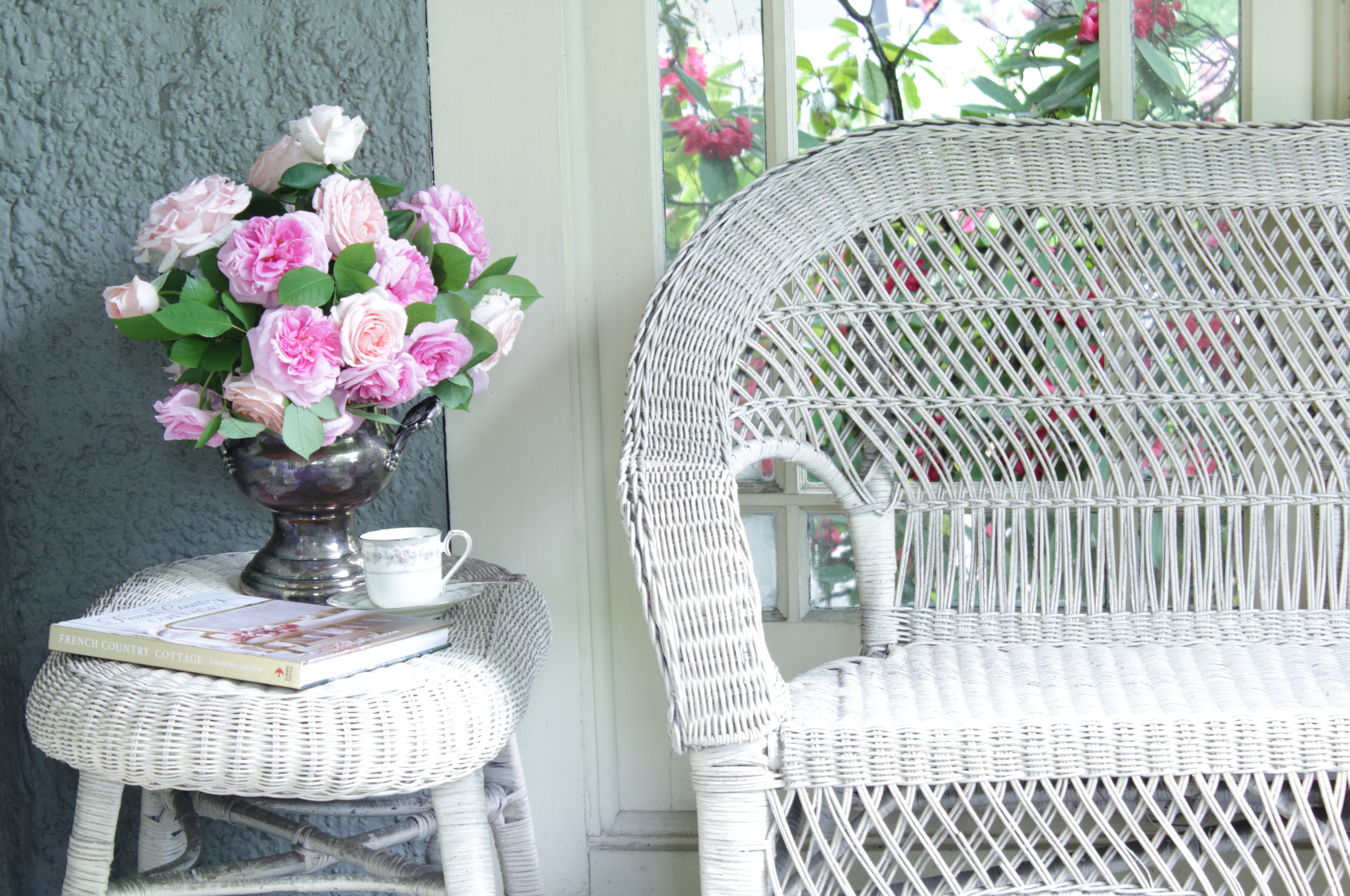 Pink & blush roses in silver wine bucket on wicker table next to loveseat on porch