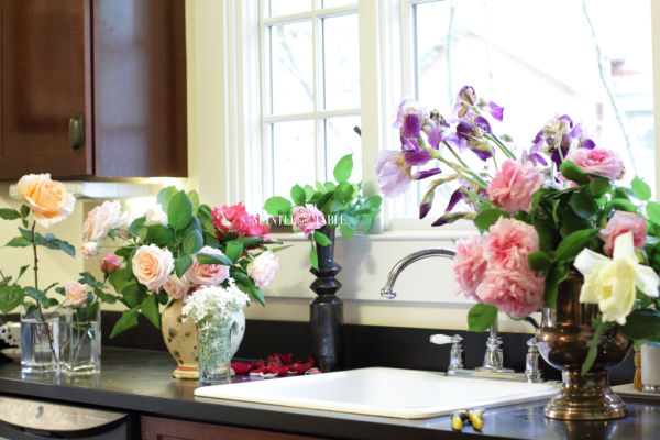 Lots of varieties of cut fresh flowers in vases on the kitchen counter. With sink.