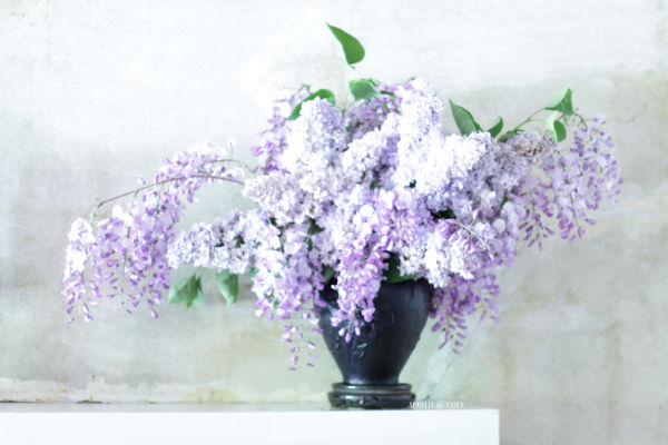 Black amethyst vase of lavender lilacs & wisteria on white mantel