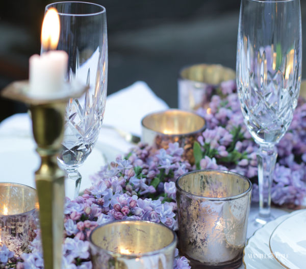 Candles, crystal and lilac garland on white linen tablecloth
