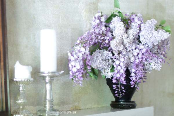 Lilacs & wisteria in black amethyst glass vase on white mantel with silver mercury glass candle holders